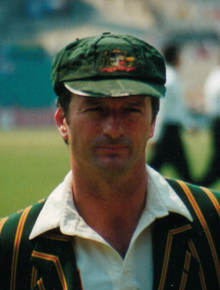 Cricketer Steve Waugh đội mũ cricket xanh rộng thùng thình và áo blazer sọc, kiểu đại học mang màu sắc quốc gia của Úc.